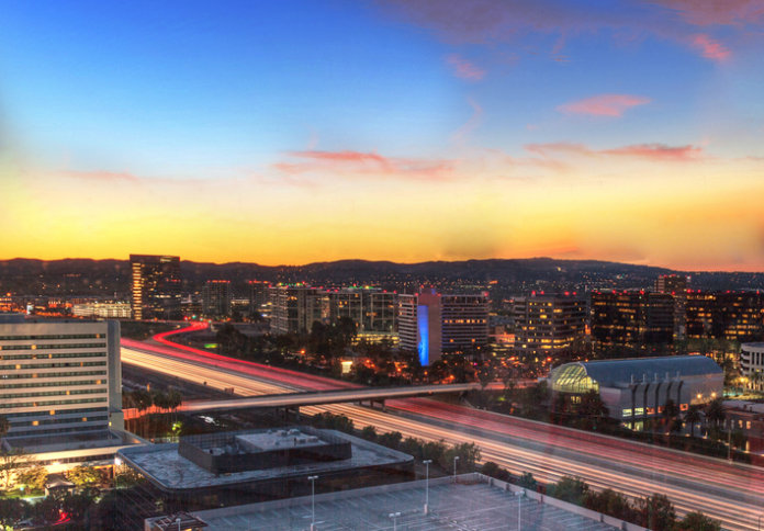 Sunrise over a highway in Irvine, California as headlight trails move through the roadways.